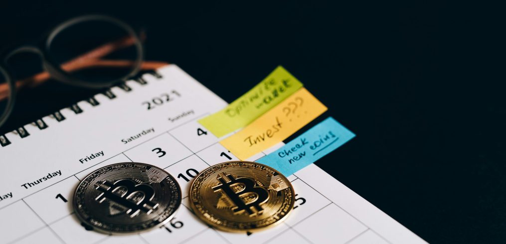 Bitcoin coins placed on a calendar with sticky notes for investment planning.